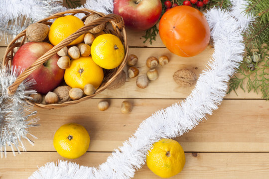 Tangerines in Christmas decor with Christmas tree, nuts and apples on light wooden background