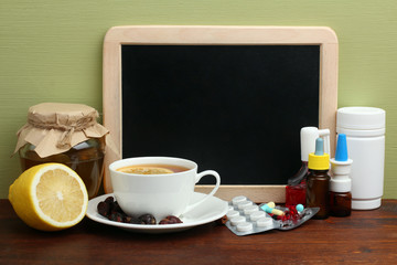 a Cup of tea with lemon and a jar of honey near the Board for writing and a lot of drugs on wooden table on green background