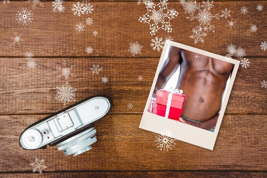 Photo of shirtless man holding gift on wooden table