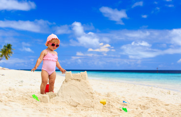 cute little girl building sandcastle on beach