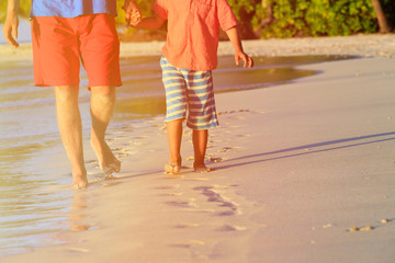 father and son walking on beach leaving footprint in the sand