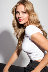 Fototapeta premium Awesome caucasian attractive sexy professional female model with blond hair posing in studio wearing white shirt and black ripped jeans, smiling, isolated on white background