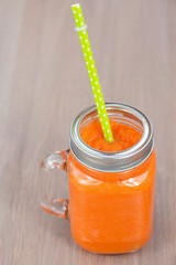 Healthy carrot smoothie in a jar with tube wooden background