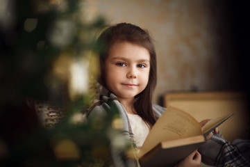 little cute girl sitting near christmas tree and reading book