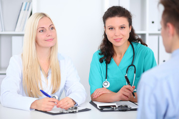 Two confident friendly female doctors sitting at the table and listen to the patient's history . Medical and health care concept