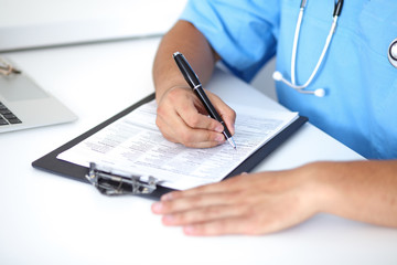 Fototapeta premium Portrait of unknown male surgeon doctor holding his stethoscope and filling up medical prescription