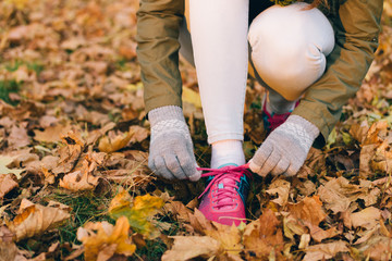 Woman tying shoelaces on sneakers during an autumn walk in the p