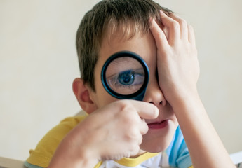 big blue eyes through a magnifying glass. handsome boy playing with a magnifying glass bringing it...