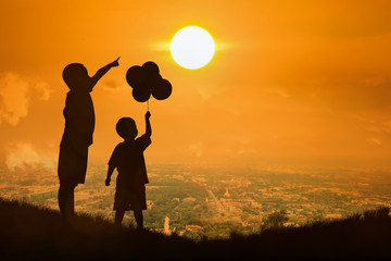 silhouette of asian little boy point to the sun at sunset backgr
