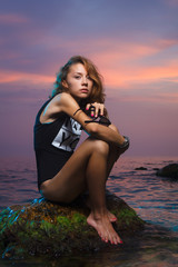 Teen girl sitting on stone fashion shoot at sunset beach