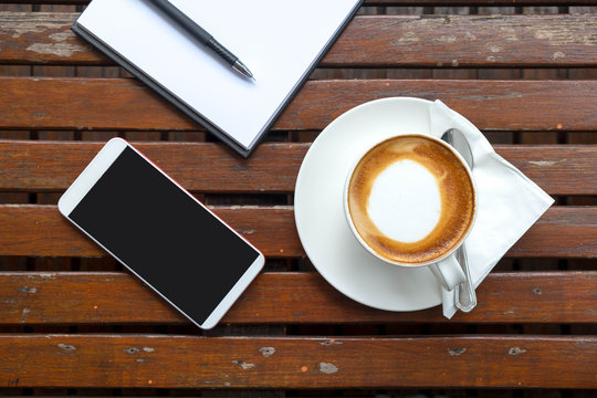 cup of coffee with white paper and smartphone put on wooden table