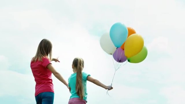 Mother and daughter with balloons turned and looking at the camera. Mother and daughter holding hands and looking at distance