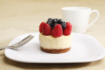A cheesecake pastry in a dish with fork and coffee or tea cup.