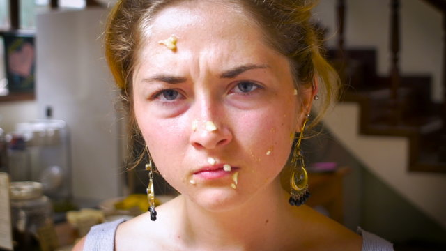 An attractive, young woman, wipes and blows bananas off her face as she looks irritated, pissed and annoyed while looking at the camera.