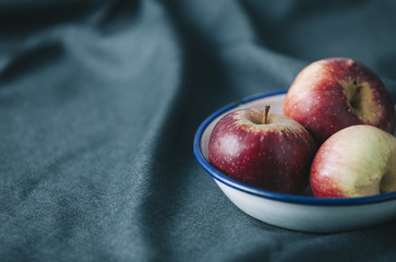 fresh red apples in enameled plate, on dark fabric
