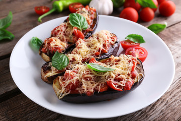 Dish of eggplant with cherry tomatoes and cheese in white plate on wooden table, closeup