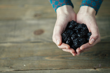 hands of a lady with full of dried plums on wooden background