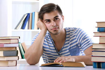 Young man reading book at table in room