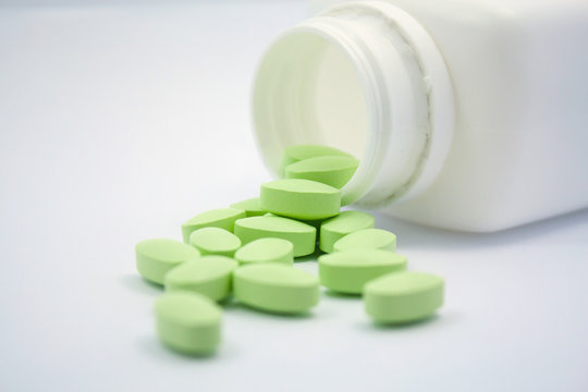 Green Pills And Pill Bottle On White Background