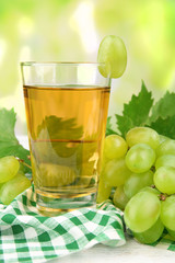 Glass of grape juice on table with checkered napkin on light blurred background
