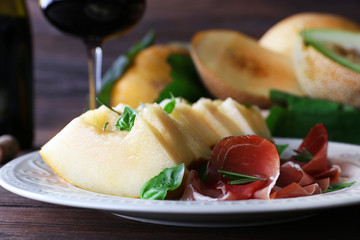 Melon with prosciutto of Parma ham on wooden table, closeup