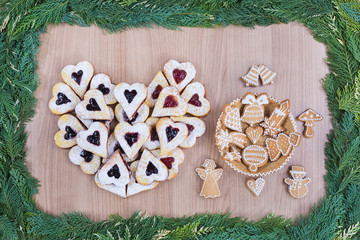 Homemade decoration jam shortbread cookies and honey cookies on christmas theme with frame by pine tree twigs on wooden background .