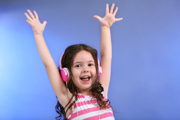 Attractive little girl with pink headphones on blue background