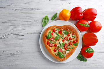 Delicious heart shaped pizza with vegetables on wooden background
