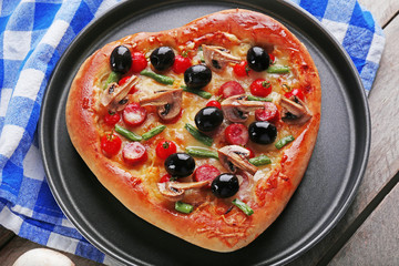 Heart shaped pizza on pan and blue checked cotton serviette on wooden background