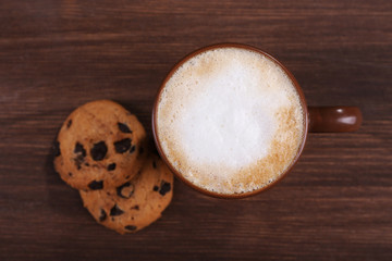 Cup of coffee with milk foam and cookies on wooden background