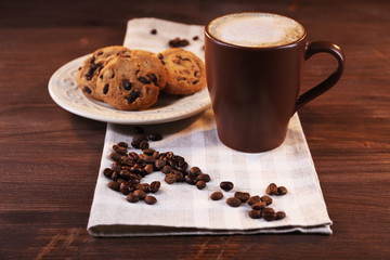 Cup of coffee with roasted coffee beans around and biscuit on cotton serviette on wooden  background