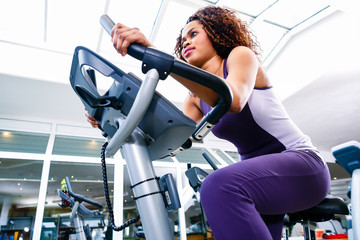 African woman in gym spinning on fitness bike