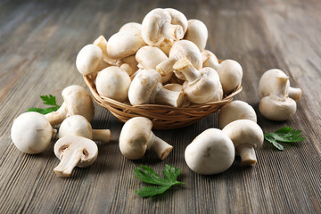 Champignon mushrooms in a basket and parsley on grey wooden background