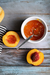 Tasty jam in the bowl, ripe peaches and fresh buns on wooden background close-up