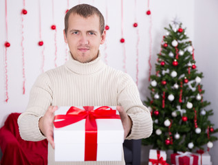 Obraz na płótnie Canvas young man giving christmas present box over christmas background