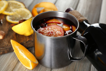 Delicious mulled wine in a mug with citruses on decorated wooden background, close up