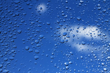 Rain drops on window with blue cloudy sky in background