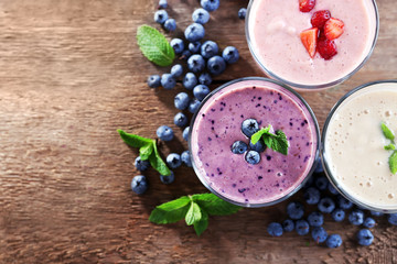 Tasty blueberry, strawberry and milk yogurts with berries and mint around on wooden background
