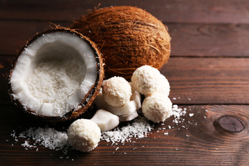 Candies in coconut flakes and fresh coconut on dark wooden background
