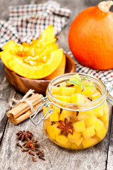 Marinated  pumpkin dices in a glass container on a wooden table.