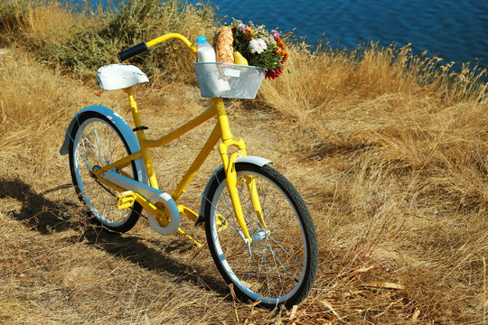 Beautiful yellow bicycle with bouquet of flowers, milk bottle and bread in basket, outdoors