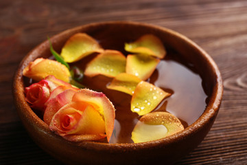 Beautiful orange rose and petals in a bowl of water on wooden background