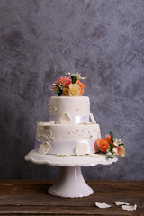 White wedding cake decorated with flowers on wooden table against grey background