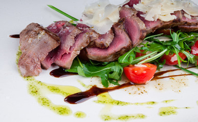 Medium rare steak served on a plate with cherry tomatoes and arugula. On top of it is grated parmesan cheese.