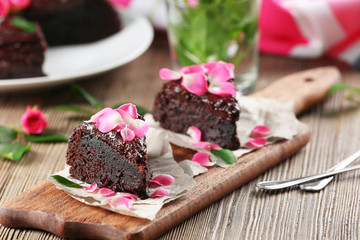 Piece of chocolate cake decorated with flowers on brown wooden table