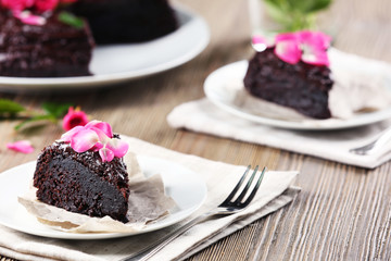 Piece of chocolate cake decorated with flowers on brown wooden table