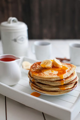Pancake with banana and syrup on a white wooden trays and cups of tea
