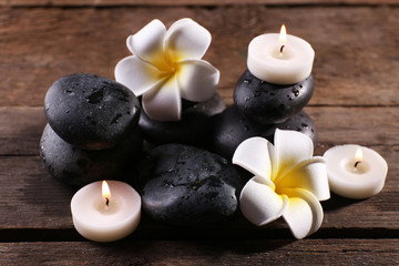 Relaxing composition with exotic fragipani flower, pebbles and candles on wooden background