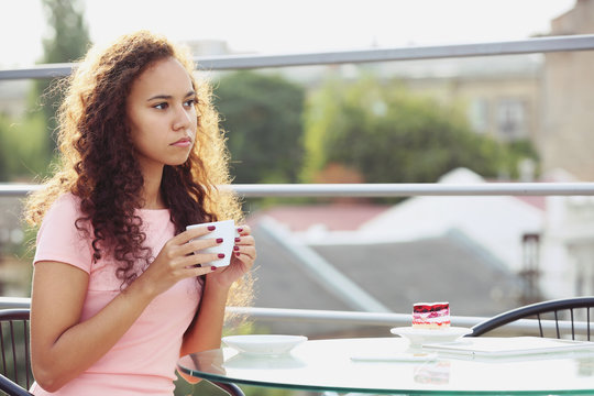 Pretty young woman in pink dress drinking coffee at summer terrace