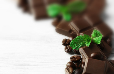 Black chocolate pieces and mint leaves on color wooden background